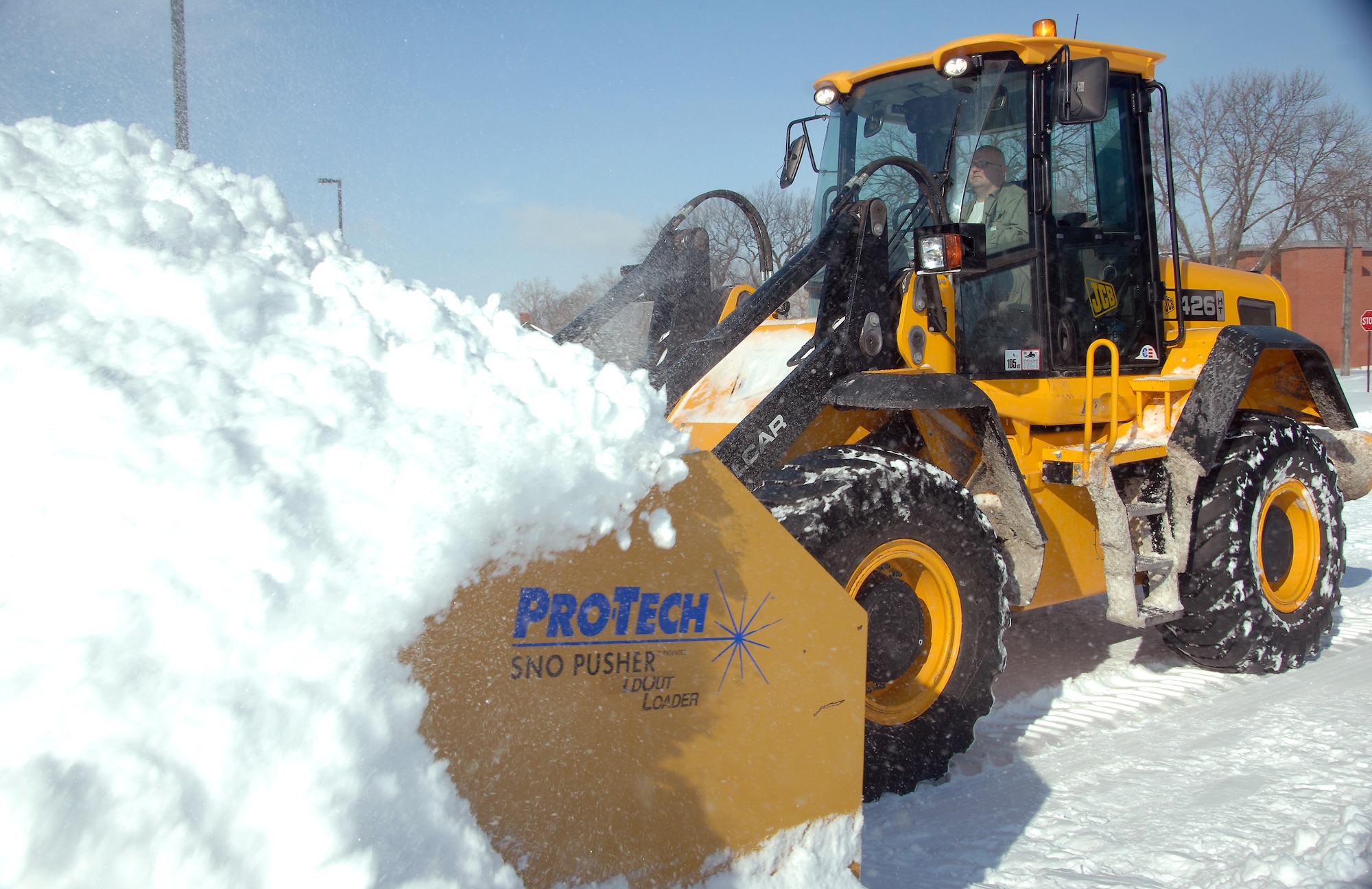 Matt Rix, an airfield clearing operator from the 55th Civil Engineering Squadron, operates a front-end loader with a pusher blade to clear snow from the parking lot of the Base Exchange at Offutt Air Force Base, Neb., Feb. 22. Offutt received eight inches of accumulation with the storm. (U.S. Air Force photo by Delanie Stafford/Released))