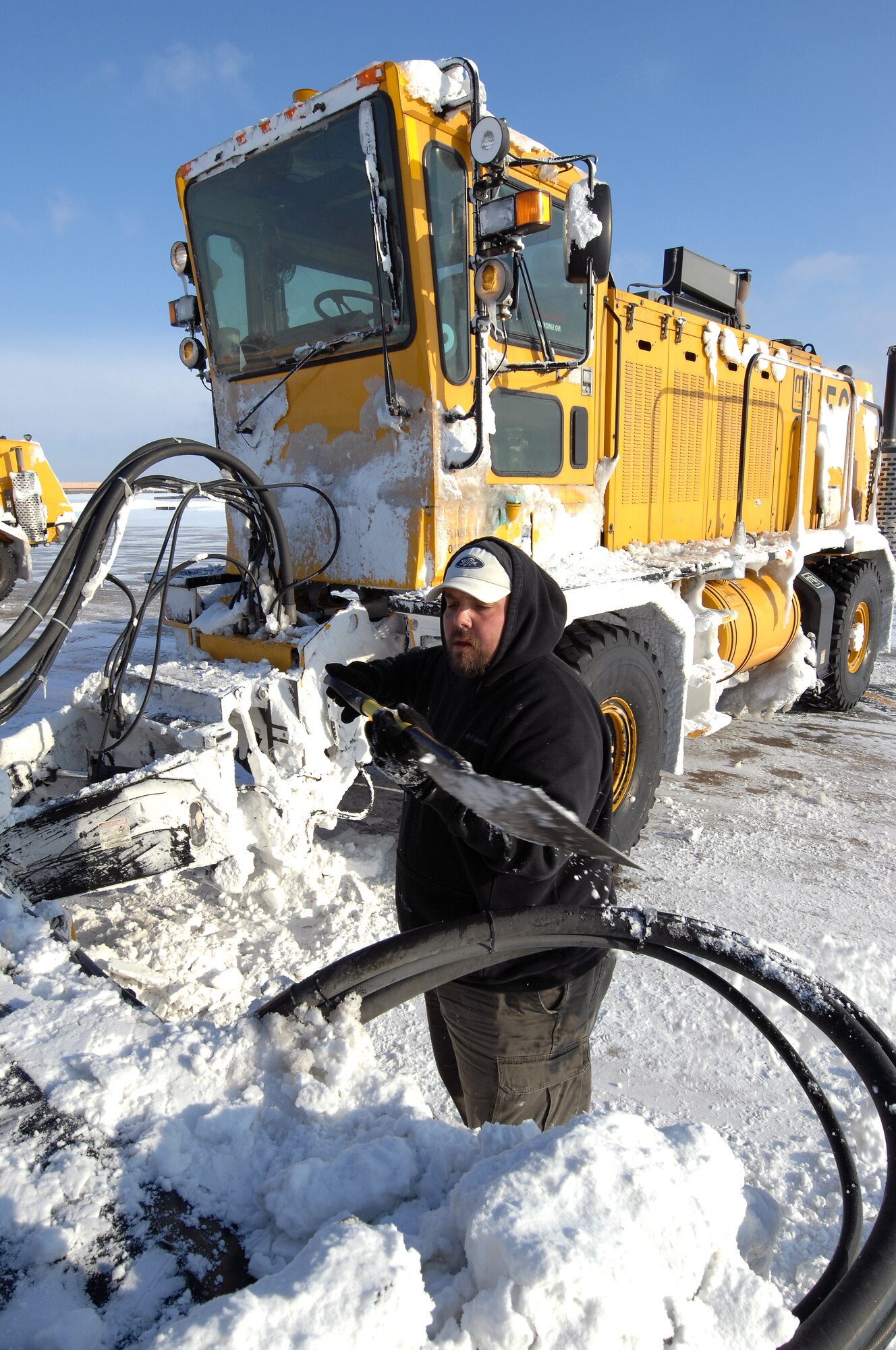 Phil Wertz, an airfield clearing operator from the 55th Civil Engineering Squadron, uses a shovel to remove compacted snow from his high-speed broom during a preventive maintenance break. Taylor was working alongside other operators to remove eight inches of snow that accumulated at Offutt Air Force Base, Neb., Feb 22. (U.S. Air Force photo by Delanie Stafford/Released)