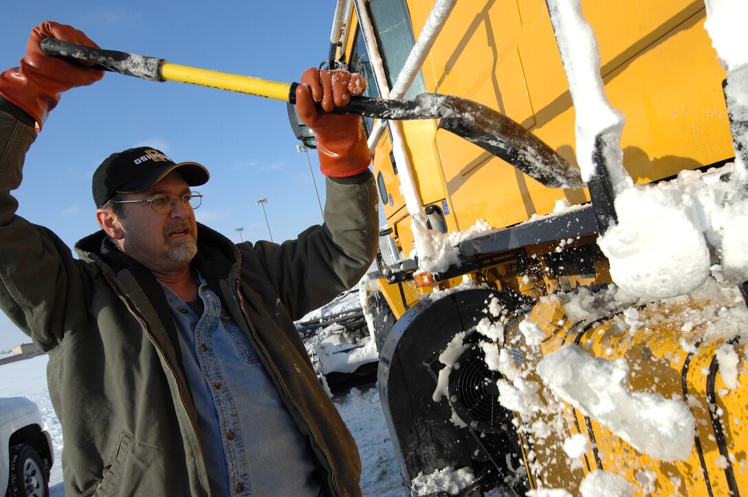 Steve Taylor, an airfield clearing operator from the 55th Civil Engineering Squadron, uses a shovel to remove compacted snow from his high-speed broom during a preventive maintenance break. Taylor was working alongside other operators to remove eight inches of snow that accumulated at Offutt Air Force Base, Neb., Feb 22. (U.S. Air Force photo by Delanie Stafford/Released)