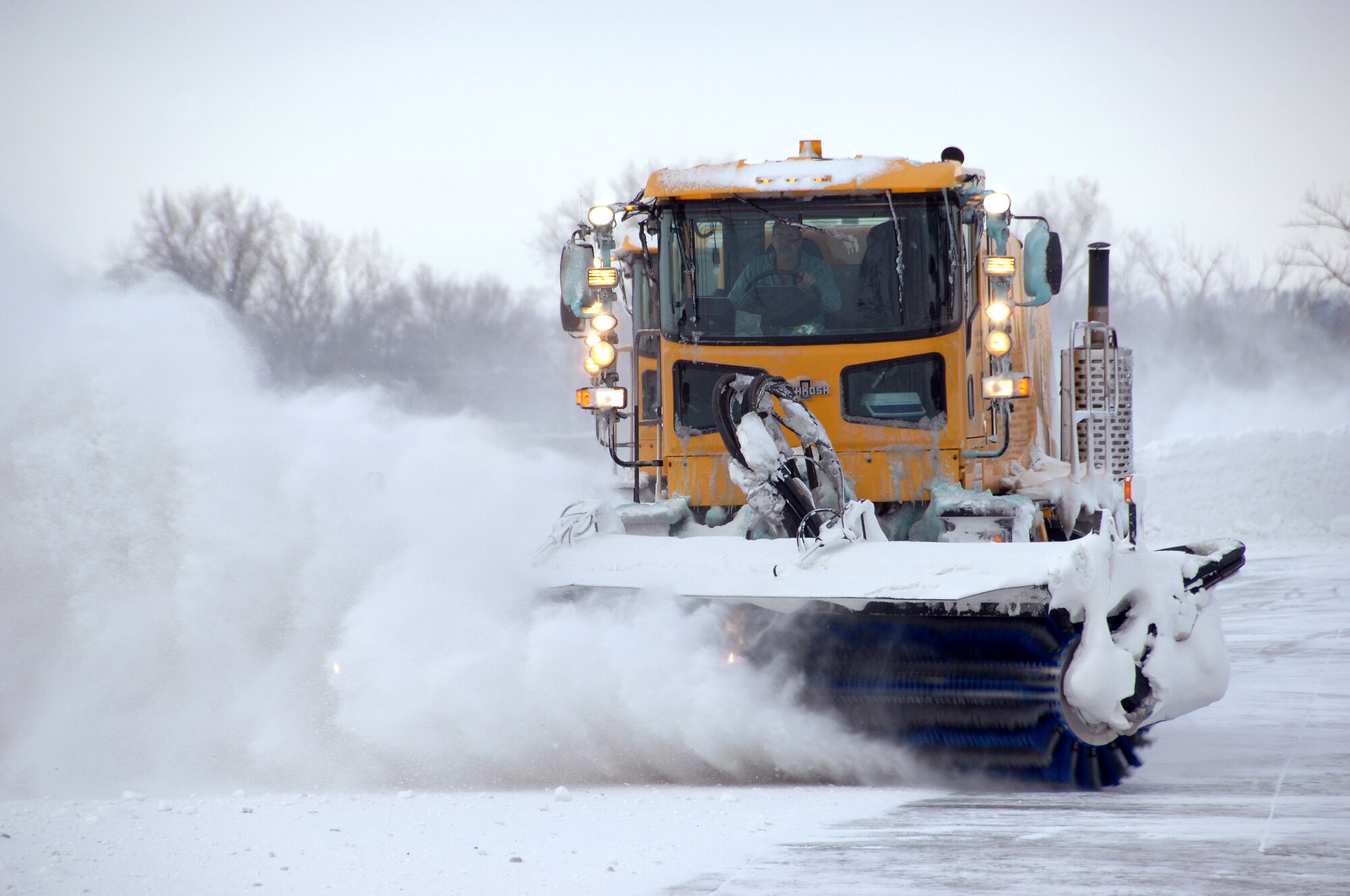 Steve Taylor, an airfield clearing operator from the 55th Civil Engineering Squadron, operates a high-speed broom while sweeping compacted snow from the lower aircraft ramp of Offutt Air Force Base, Neb., Feb. 22. Offutt received eight inches of accumulation with the storm. (U.S. Air Force photo by Delanie Stafford/Released)