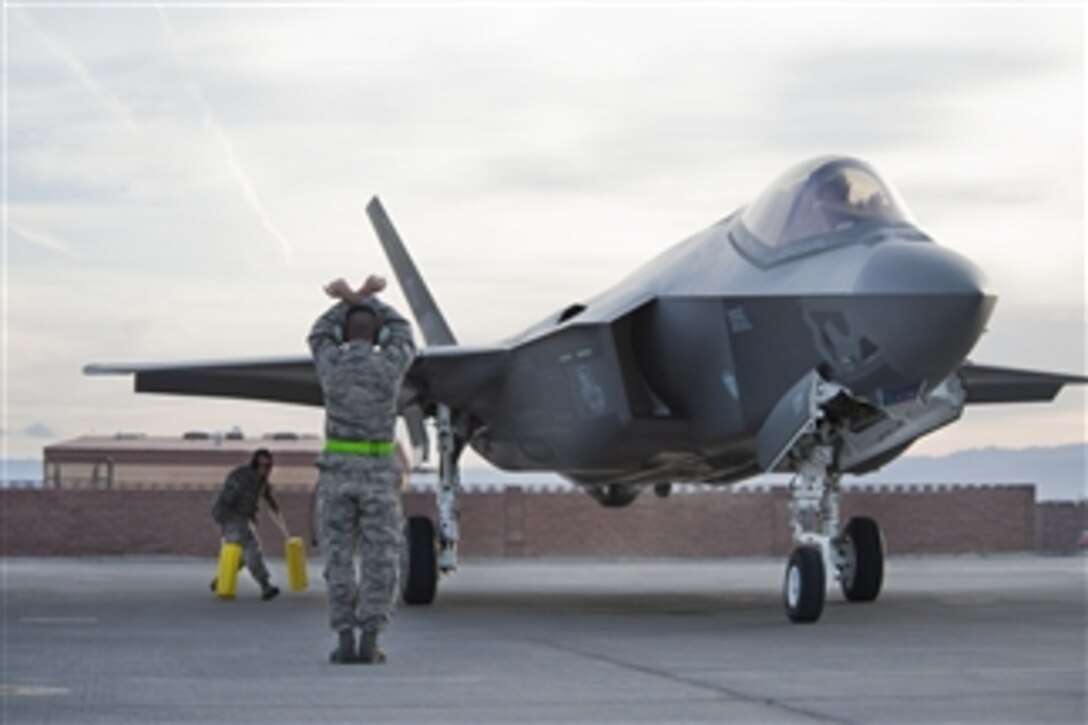 One U.S. Air Force airmen directs the pilot of an F-35 Lighting II while another places chocks around the aircraft’s wheel at Nellis Air Force Base, Nev., on March 6, 2013.  The first two aircraft will be assigned to the 422d Test and Evaluation Squadron.  