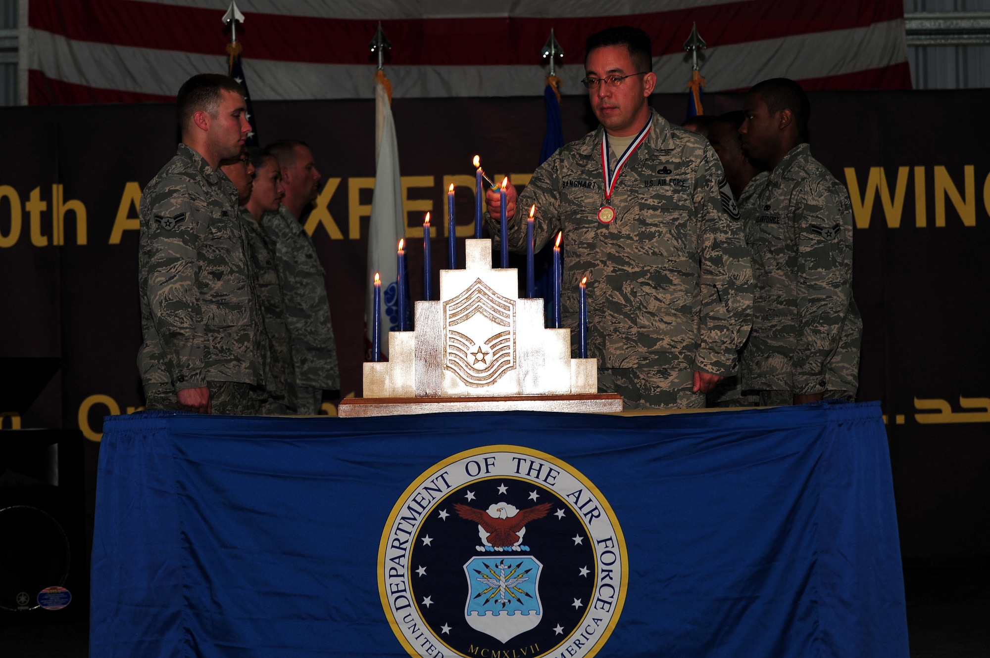 U.S. Air Force Senior Master Sgt. Jay A. Banghart, 380th Expeditionary Aircraft Maintenance Squadron KC-10 Extender aircraft maintenance unit superintendent, lights the candle representing the rank of chief master sergeant during the Chief Master Sergeant Induction Ceremony in his honor at an undisclosed location in Southwest Asia Mar. 1, 2013. The nine candles symbolically represent each enlisted grade in the Air Force and were lit by Airmen currently wearing those grades in Banghart's unit. Banghart will pin on the highest enlisted rank on April 1, 2013. (U.S. Air Force photo by Tech. Sgt. Christina M. Styer/Released)