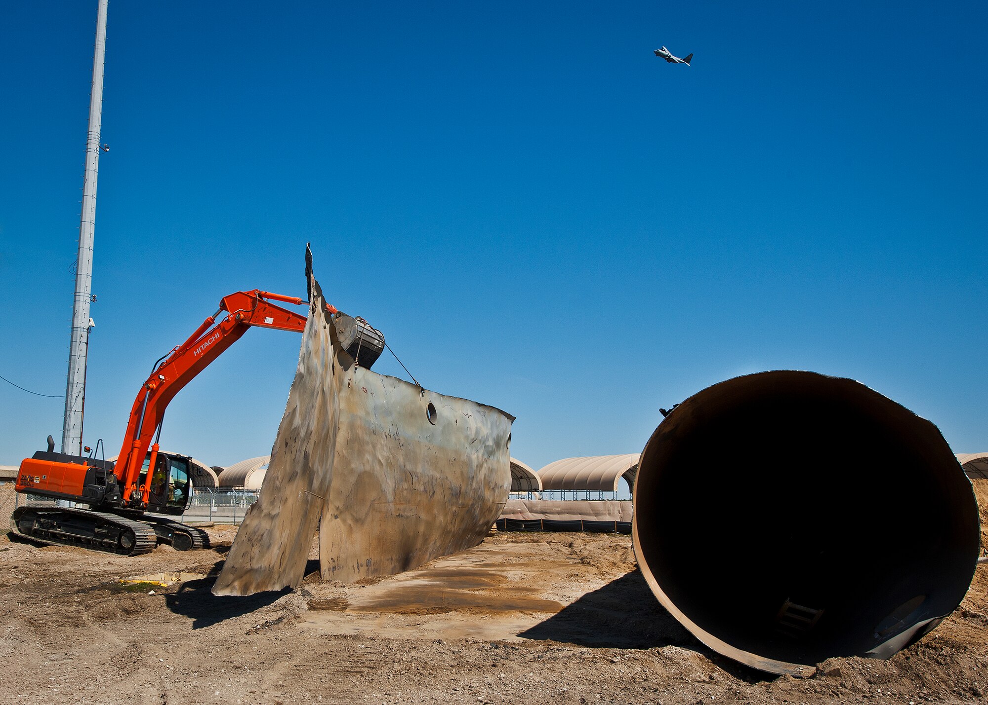 An excavator picks up a flattened piece of a 50,000 gallon underground fuel storage tank as a C-130 flies overhead near the 33rd Fighter Wing March 11 at Eglin Air Force Base, Fla.  The tank was one of four removed from the area.  The systems have been in place since 1959 and formerly used to refuel 33rd FW aircraft until recently.  The new fuel storage system is already in place and increases the wing's capacity to more than a million gallons of JP-8 for the F-35s.  (U.S. Air Force photo/Samuel King Jr.)