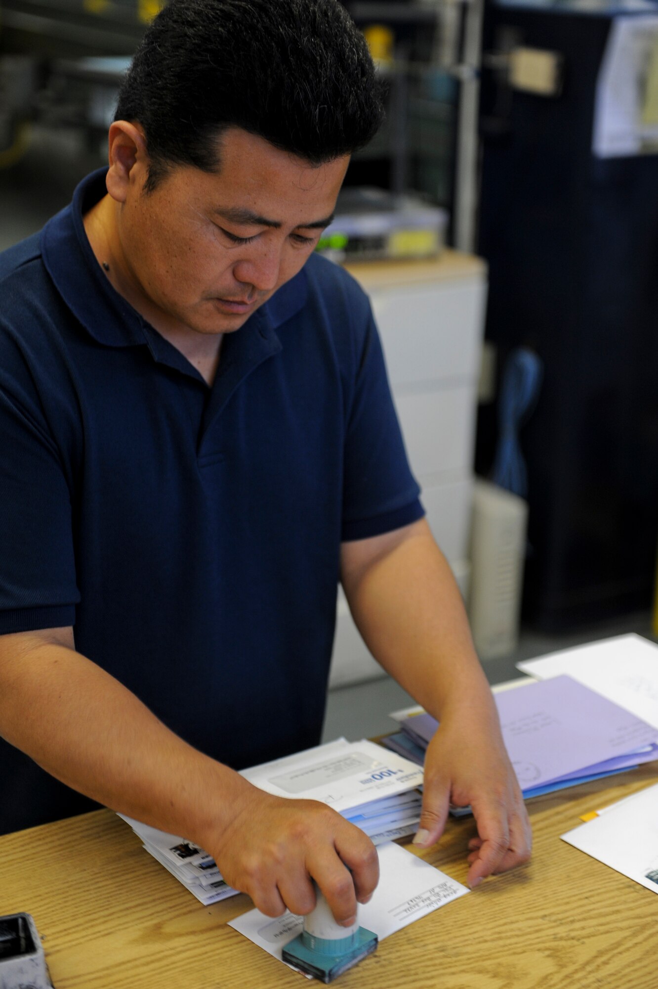 Hiroyusu Kuda, Detachment 3 Pacific Air Forces Air Postal Squadron postal specialist, stamps a piece of mail on Kadena Air Base, Japan, March 11, 2013. PACAF's Detachment 3, APS, serves as the Department of Defense's sole agency for air transport of military mail to and from Okinawa, and manages mail-related customs and inspections. (U.S. Air Force photo/Airman 1st Class Justin Veazie)