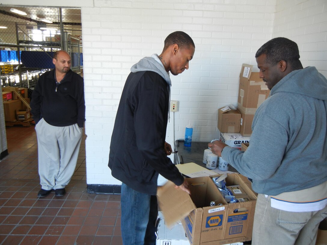 From left, Oren Ancar, supervisor of the Industrial Supply Center, looks on as Derek Obi, mobile equipment servicer for Motor Transport Maintenance Section, picks up an order of filters, cables, tender springs and marker lights from Jeffery Johnson, material handler with the Industrial Supply Center on March 4. The center now purchases all parts and supplies for both Motor-T Maintenance and Facilities Maintenance. 