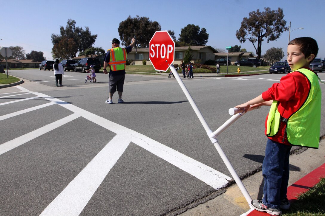 Jordan Pendexter, a 10-year-old student of North Terrace Elementary School, and a faculty supervisor hold traffic to help students cross the street, Mar. 12. As the faculty supervisor blows the whistle, Pendexter lowers the stop sign to signal the oncoming traffic.