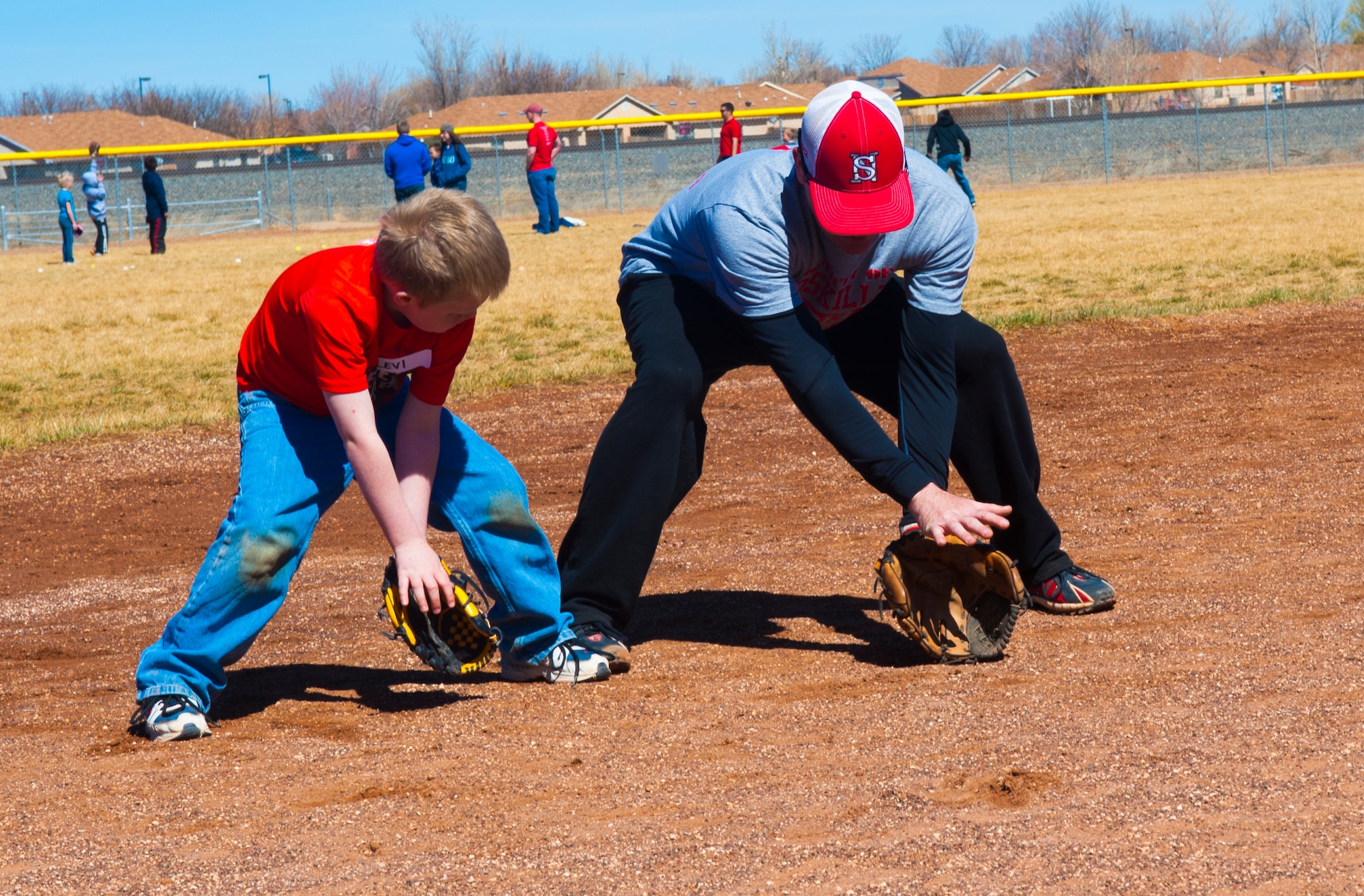 A sports clinic volunteer helps a child with fielding fundamentals on the baseball field at Cannon Air Force Base, N.M., March 11, 2013. Various base organizations recently sponsored free baseball and softball clinics for local youth. (U.S. Air Force photo/Airman 1st Class Xavier Lockley)