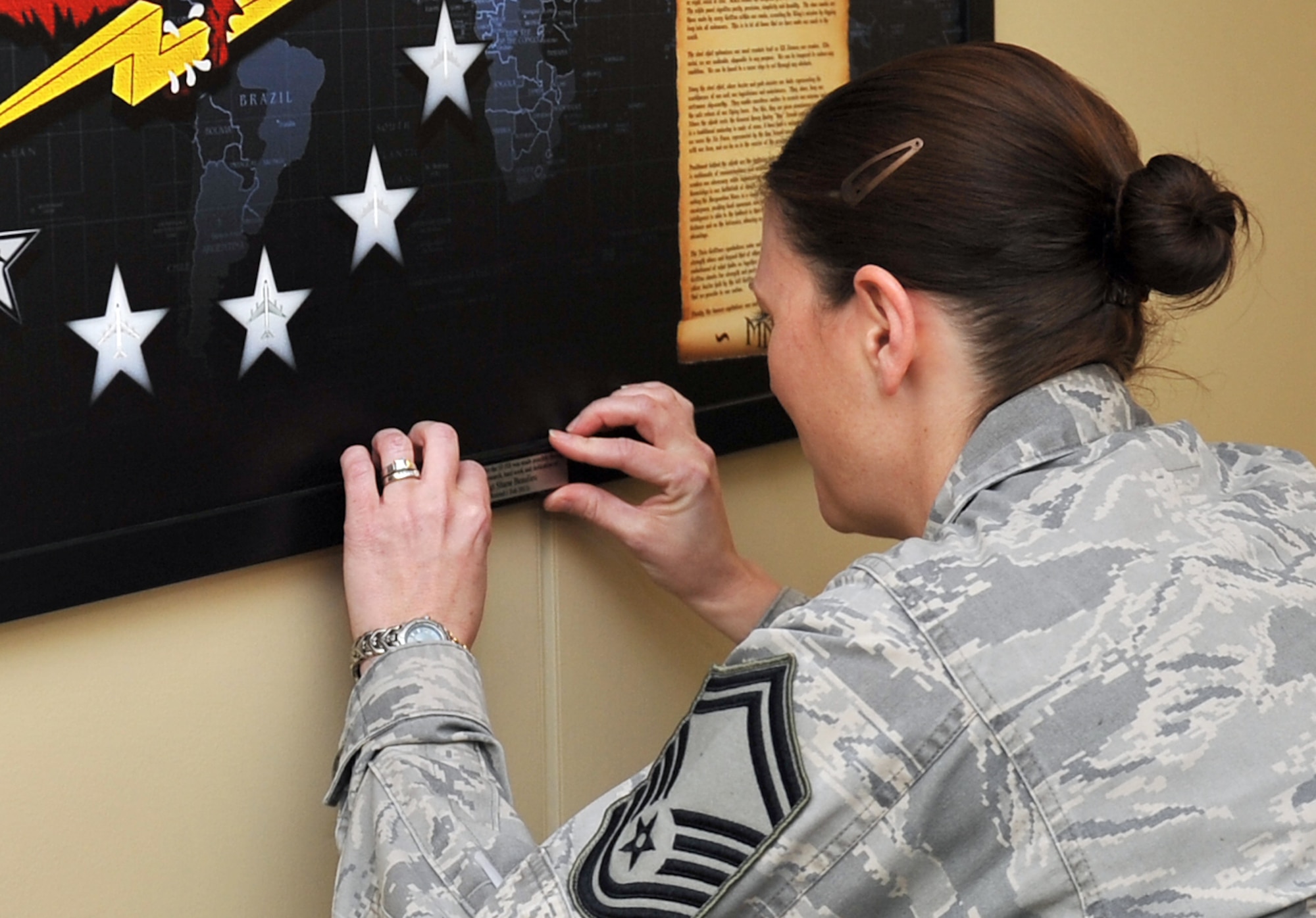 U.S. Air Force Senior Master Sgt. Melissa Poole-Knight, a flight chief with the 55th Intelligence Support Squadron, carefully places the identification placard on the newly created squadron coat of arms in the hallway of the 55th Operations Group on Offutt Air Force Base, Neb. U.S. Air Force Lt. Col. Ty Gilbert, 55th ISS commander, was also on hand to help mount the work which was created and donated by Retired U.S. Air Force Master Sgt. Shane Beaulieu. (U.S. Air Force photo by Jeff W. Gates/Released)