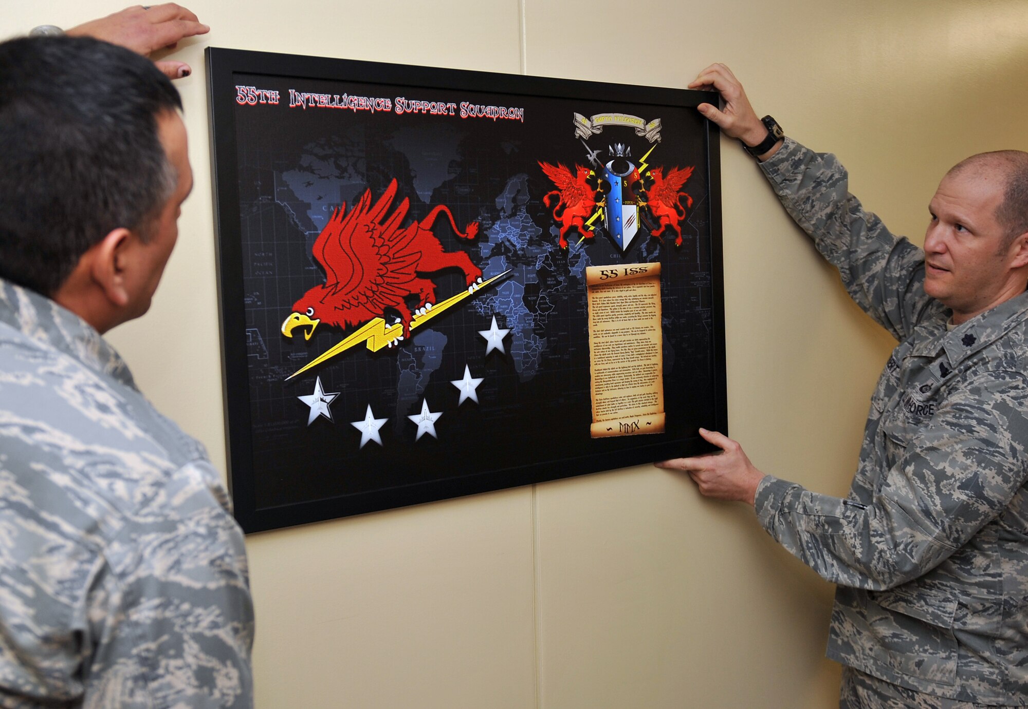 (left to right) U.S. Air Force Maj. Gil Moncada, 55th Intelligence Support Squadron director of logistics, and U.S. Air Force Lt. Col. Ty Gilbert, 55th ISS commander, mount the newly created squadron coat of arms.  The work was created and donated by retired U.S. Air Force Master Sgt. Shane Beaulieu as a dedication to the 55th ISS. The piece was hung in the hallway of the 55th Operations Group on Offutt Air Force Base, Neb. (U.S. Air Force photo by Jeff W. Gates/Released)