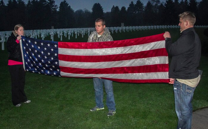 (Left) Airman 1st Class Meghan Servais, 17th Airlift Squadron loadmaster, (center) Airman 1st class James Moss, 17th AS loadmaster and 1st Lt. Daniel Klepper, 17th AS pilot, perform a Retreat Ceremony and fold a U.S. American Flag during a trip to the Luxembourg American Cemetery, Luxembourg. More than five thousand American service members, who were killed in action during World War II, including Gen. George Patton, are buried here. (Courtesy photo)