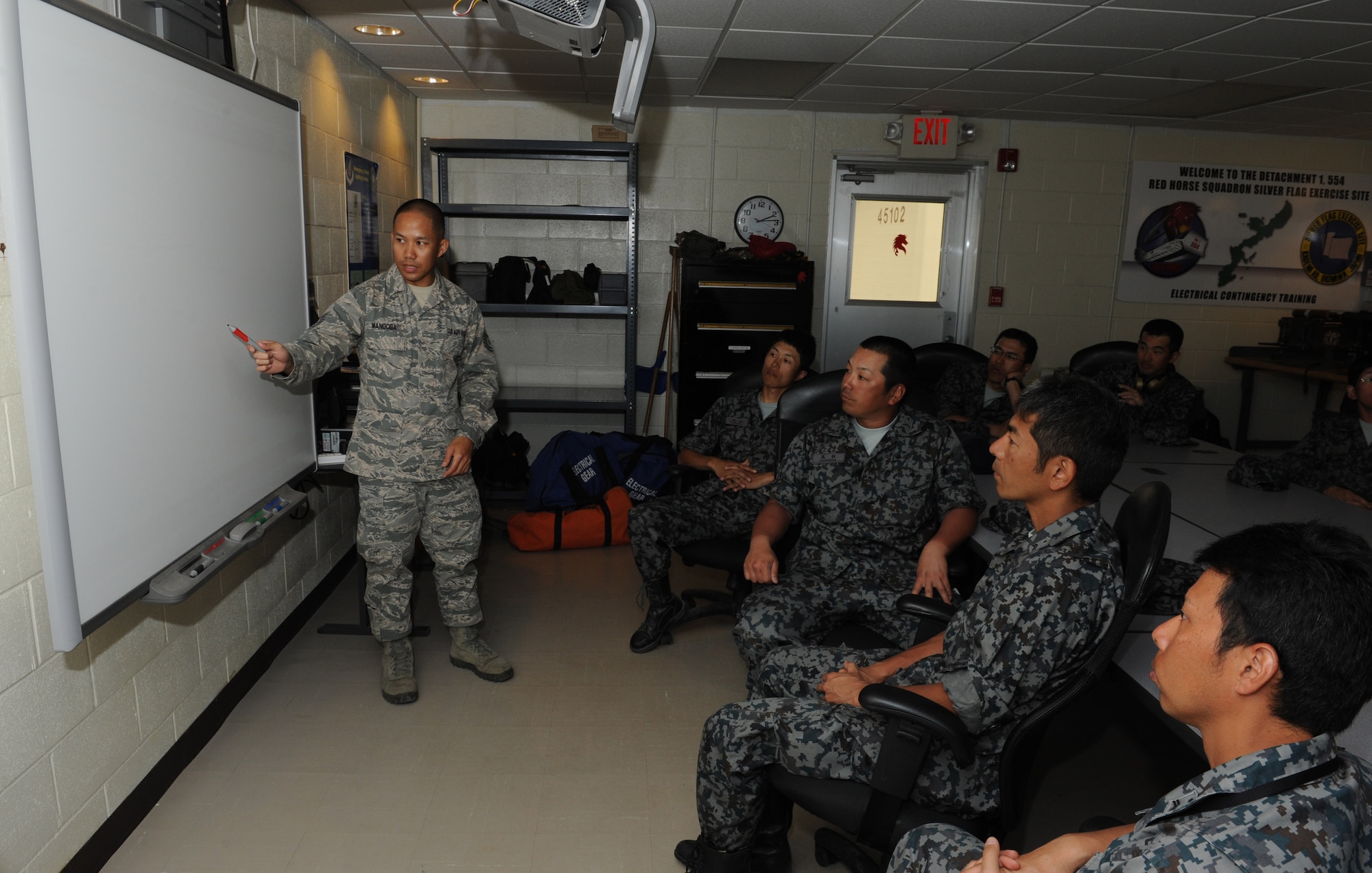 U.S. Air Force Tech. Sgt. Carlo Mangoba, Detachment 1 554th RED HORSE Squadron NCO in charge of electrical and Silver Flag contingency instructor, instructs Japan Air Self Defense Force members on electrical line diagrams on Kadena Air Base, Japan, March 11, 2013. Mangoba briefed the JASDF members about how the electrical diagrams work with the "training power plant," which is used to supply power during Silver Flag contingency exercises. (U.S. Air Force photo/Airman 1st Class Keith A. James)