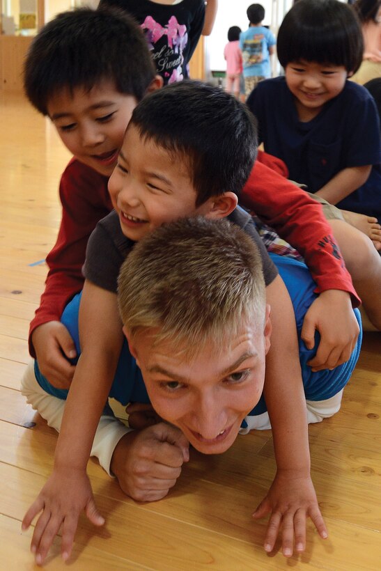 Students pile on Lance Cpl. Andrew R. Keba as he demonstrates how to low-crawl during a break in English lessons at Asunaro Nursery School March 7 in Nago. Keba is a data network specialist with Combat Assault Battalion, 3rd Marine Division, III Marine Expeditionary Force. 