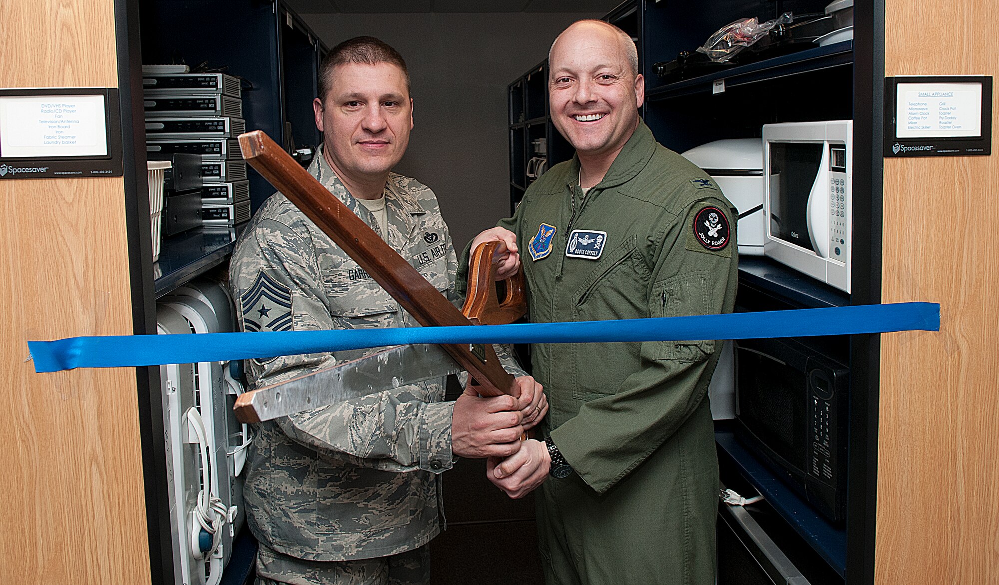 Chief Master Sgt. Michael Garrou, 90th Missile Wing command chief, and Col. Christopher Coffelt, 90th MW commander, pose with ceremonial scissors at the ribbon cutting for the Air Force Sergeants Association Loan Locker March 8. On the shelves behind them are microwave ovens, coffee makers, DVD players and other household items available for checkout. The loan locker, operated by the AFSA Cowboy Chapter and located in the Airman and Family Readiness Center building, provides needed items for families moving to, or from, F. E. Warren Air Force Base, while they are separated from their household goods. (U.S. Air Force photo by R.J. Oriez)