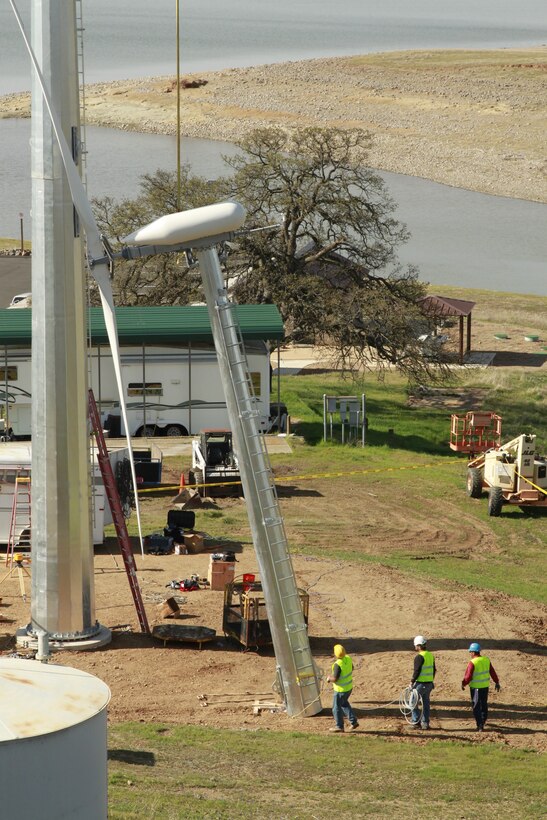 Construction workers standing near the wind turbine help put the size of the project in proportion as the top section is hoisted aloft at Black Butte Lake.
