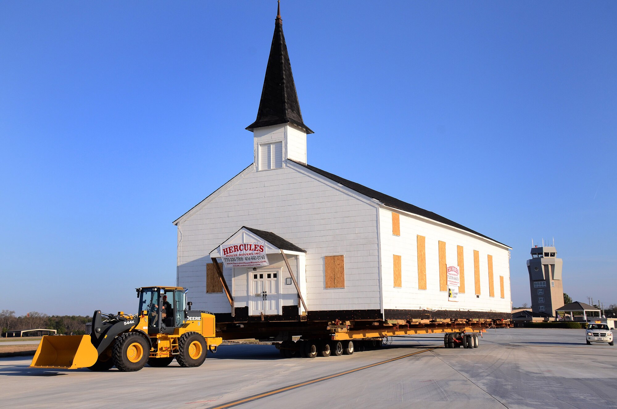 The Dobbins chapel is towed down the flight line, past the control tower, on its way to the Clay Army National Guard camp on the south side of the Dobbins runway, Dobbins ARB, Ga., March. 17. The 30 ton load is supported by several heavy steel beams, wood cribbing, and three hydrostatic dolly assemblies which are all towed by a heavy-duty front-end loader.  To meet post-9/11 security requirements, new construction of a perimeter road and parking lot at the chapel site dictated the chapel must be removed.  The private, non-profit Dobbins Chapel Foundation, 94th Airlift Wing and Georgia National Guard arrived at a solution at no cost to the government, to move the historic chapel across the base. (U.S. Air Force photo/Brad Fallin)