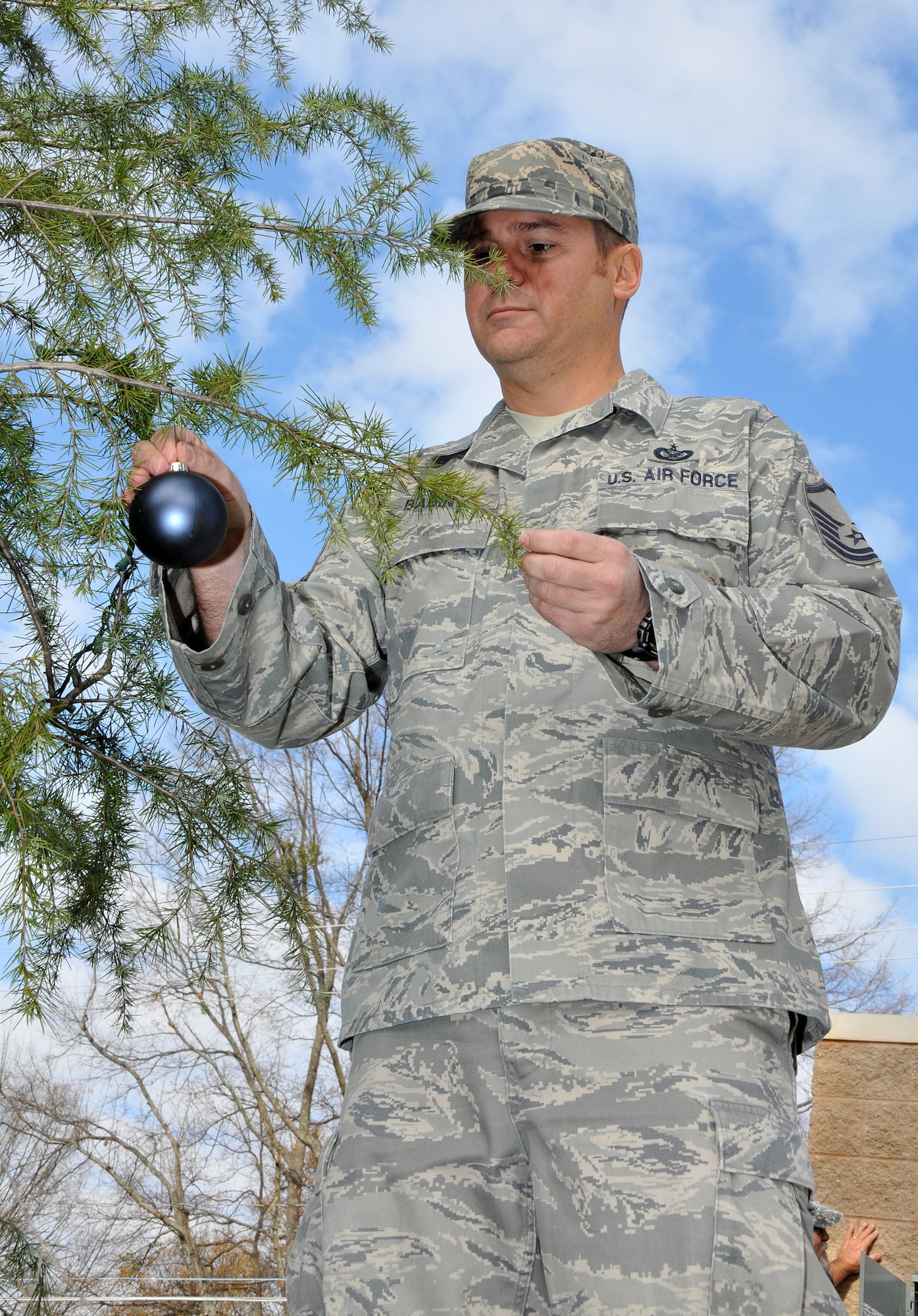 Master Sgt. Chance Babin, 94th Airlift Wing public affairs specialist, multitasks between decorating the holiday tree and mentoring young photojournalists. Members of the First Four, on behalf of Chief Master Sgt. Wendell Peacock, 94th Airlift Wing command chief, invited Dobbins Air Reserve Base personnel out to decorate the base holiday tree near the front gate, Nov. 30.(U.S. Air Force photo/Senior Airman Elizabeth Van Patten)
