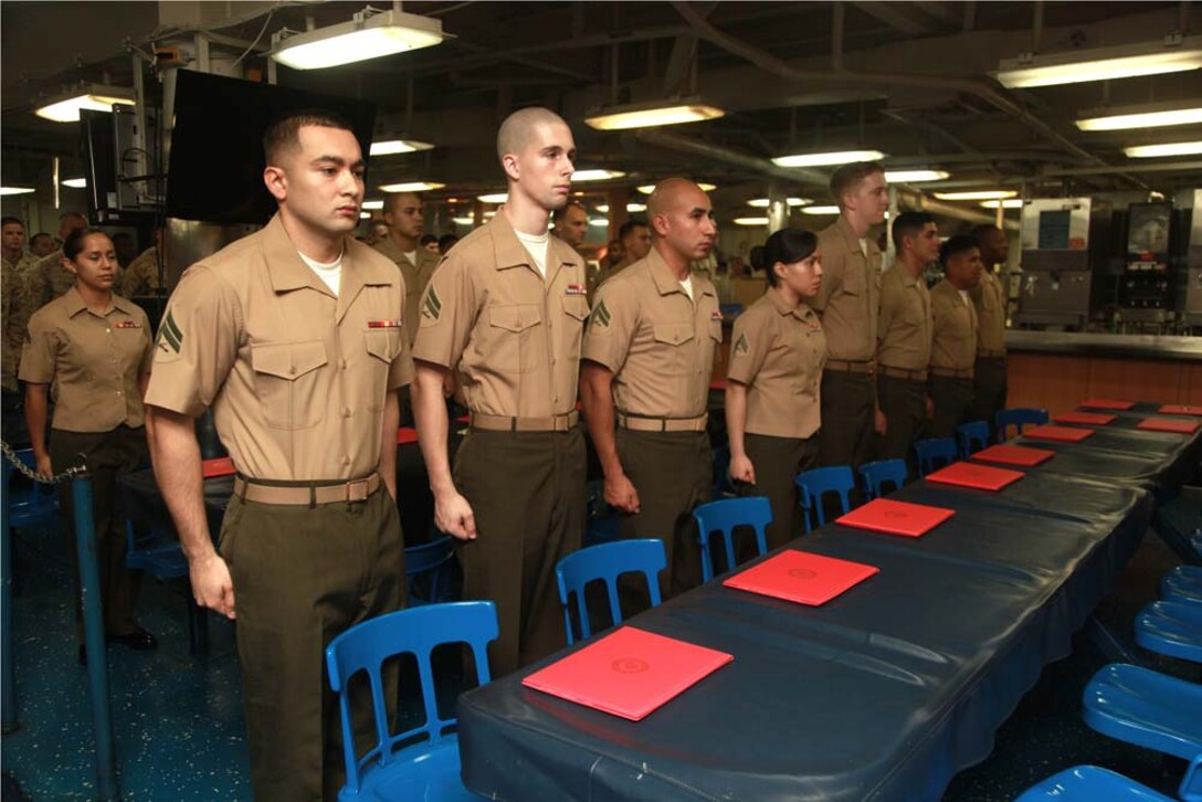 Corporals with the 15th Marine Expeditionary Unit stand at the position of attention during the playing of the Marine Corps hymn in the troop mess decks of USS Peleliu before the start of their Corporals' Course graduation, March 15. Corporals' Course is a professional military education for enlisted Marines designed to give corporals the tools to become more effective small unit leaders. The 15th MEU is deployed as part of the Peleliu Amphibious Ready Group as a U.S. Central Command theater reserve force, providing support for maritime security operations and theater security cooperation efforts in the U.S. 5th Fleet area of responsibility. (U.S. Marine Corps photo by Cpl. John Robbart III)