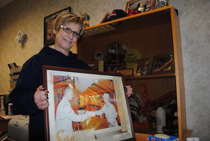 Carol Muir, Grand Forks Air Force Base Sport & Fitness Center director, holds up her favorite photo on March 15, 2013, at her office on Grand Forks AFB, N.D. Before becoming a civil servant, Muir retired as master sergeant after 23 years of service in the Air Force. The photo held up by Muir commemorates the time frame she and her son were both deployed as enlisted members to Southwest Asia. (U.S. Air Force photo/Senior Airman Luis Loza Gutierrez)