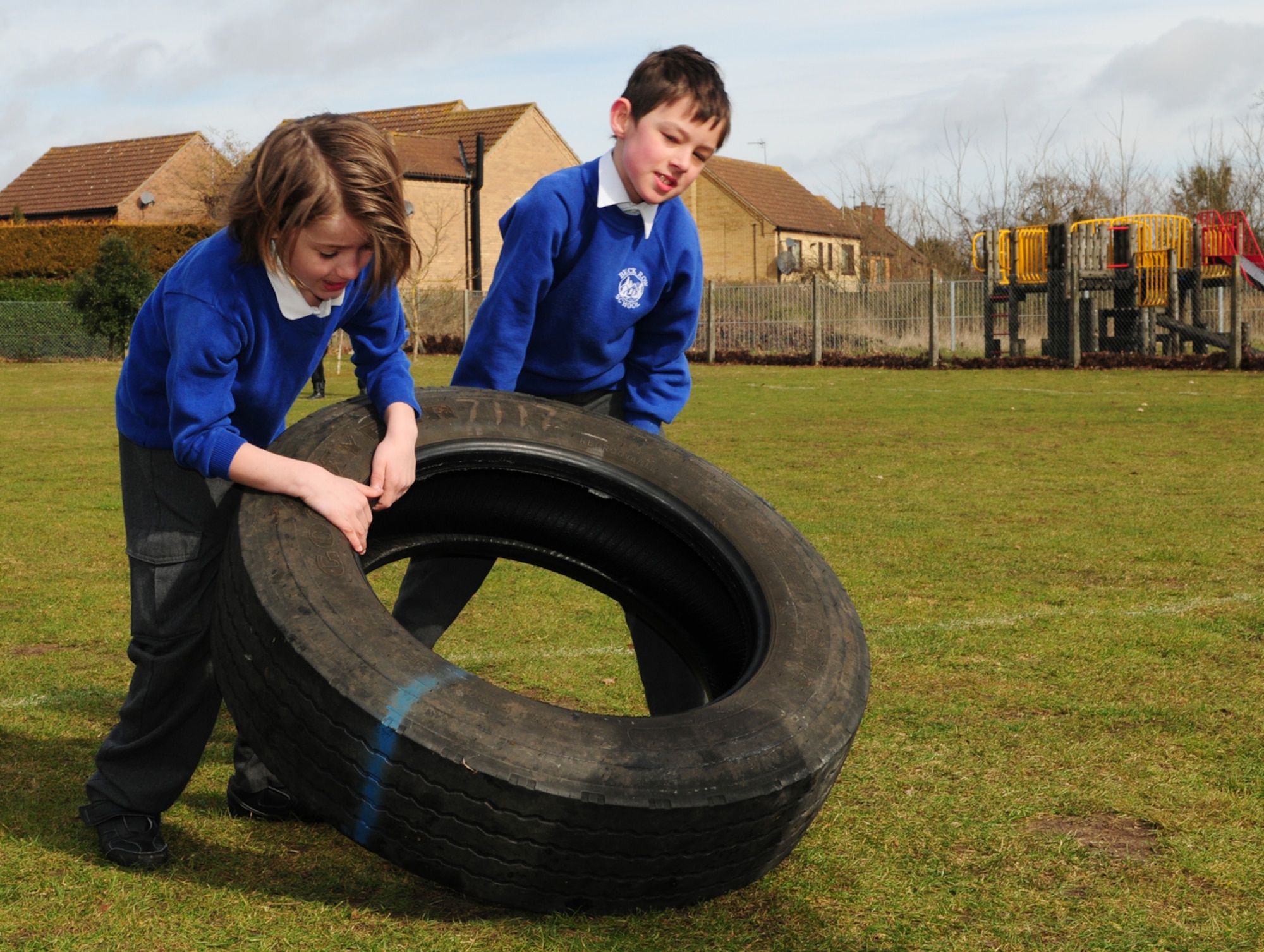Keanne and Tommy, children in Beck Row Primary School Year 4, flip a tire as part of an obstacle course set up by 100th Security Forces Squadron Airmen March 15, 2013, at Beck Row, England. Two 100th SFS Airmen played games with children, challenging them to have fun while focusing on working as a team with their classmates. Members from Team Mildenhall regularly support the local community in order to strengthen relationships and ties. (U.S. Air Force photo by Karen Abeyasekere/Released)