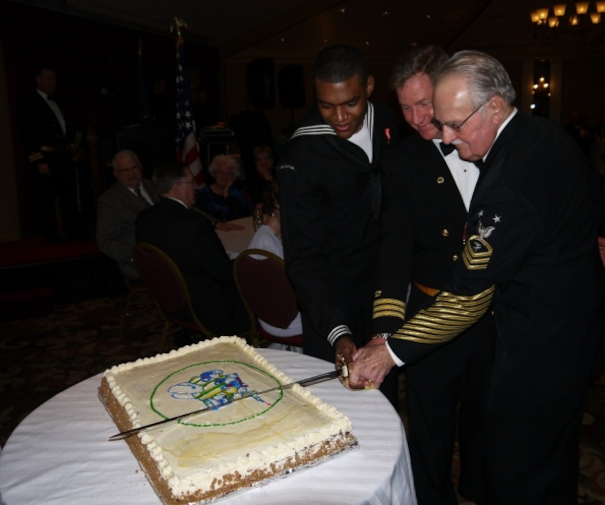 Seamen Recruit Steffan McKell, Naval Mobile Construction Battalion 21 constructionman apprentice, 19, and retired Master Chief William Starkey, 82, representing the youngest and oldest ball attendees, cut the Seabee Ball Cake at the Seabee Ball with Cmdr. William R. Mock (center), NMCB-21 commander, March 9, 2013, at the Hanover Grand Ballroom in Bethlehem, Pa. The event was the final ball for NMCB-21 and marked the 171st anniversary of Naval Facilities Engineering Command, the 146th anniversary of the Civil Engineer Corps and the 71st anniversary of Naval Construction Forces. NMCB-21 is set to decommission in September. (U.S. Navy photo by Ensign Luis Gaitan/Released)