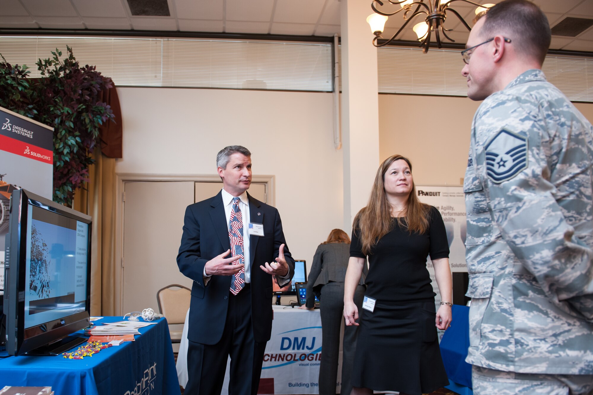 Ed Miller, Dassualt Systems Solidworks Corporation senior client executive, and Maribeth Wilson Solidworks account executive, brief Master Sgt. Michael Grant, U.S. Air Force Mobility Operations School section chief, on 3-D modeling at the 5th Annual Joint Base McGuire-Dix-Lakehurst Information Technology Expo Mar. 13, 2013, on Joint Base McGuire-Dix-Lakehurst, N.J.  The event, held at Tommy B's Community Activities Center, featured more than 50 technology vendors. Grant hails from Charlotte N.C. (U.S. Air Force photo by Russ Meseroll/Released)
