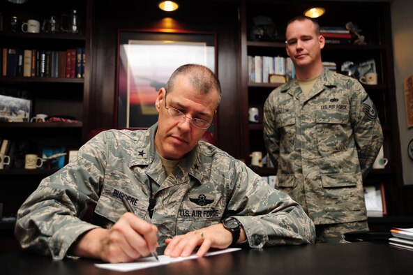 Brig. Gen. Thomas Bussiere, 509th Bomb Wing commander, signs a check for the Air Force Assistance Fund as Master Sgt. Frederick Statton, 509th Bomb Wing Staff AFAF representative, looks over his shoulder at Whiteman Air Force Base, March 19, 2013. The AFAF campaign is an annual, on-the-job fundraising appeal conducted among Air Force personnel for the benefit of Air Force members. (U.S. Air Force photo by Staff Sgt. Nick Wilson/Released) 
