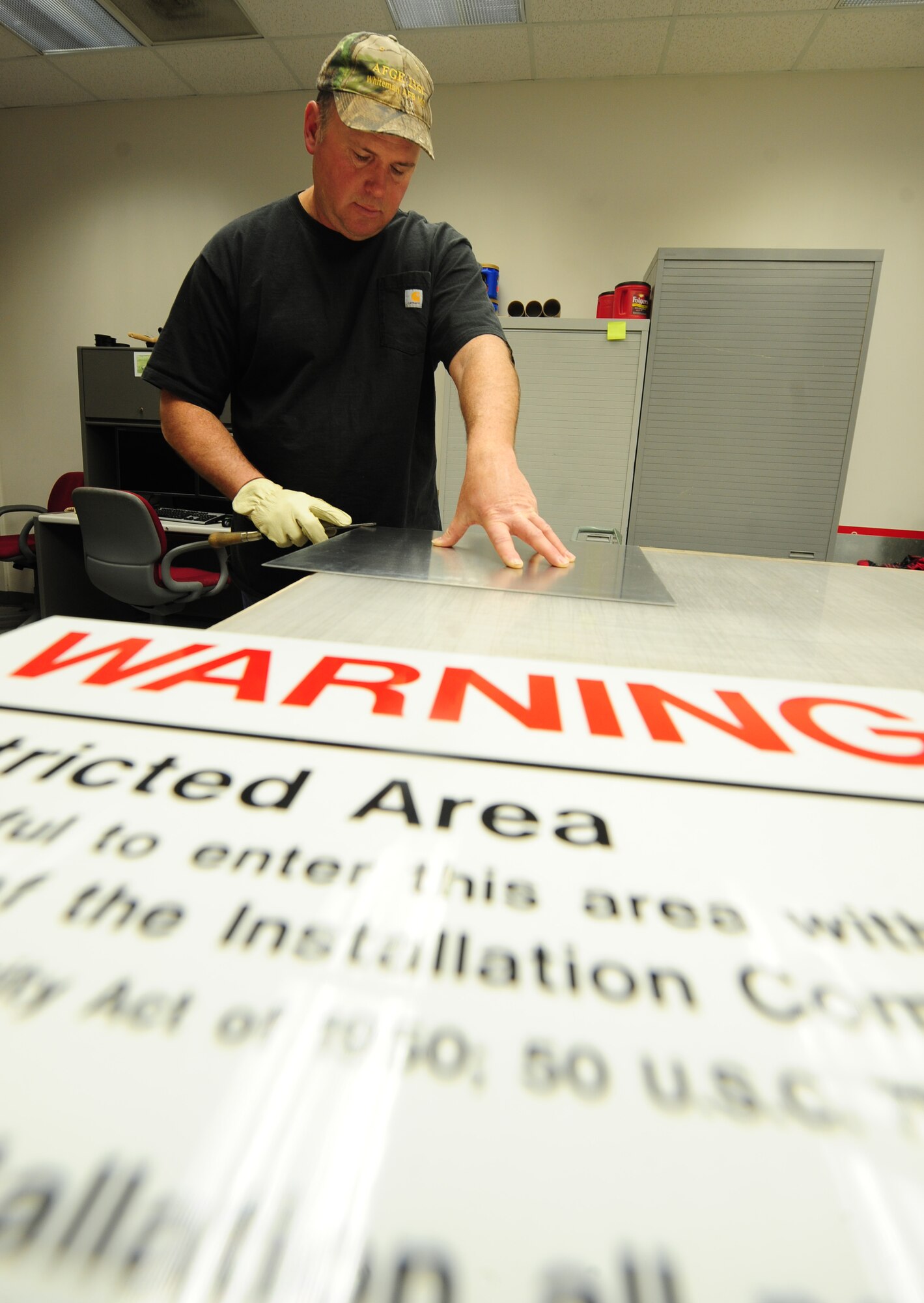 Bernard Jones, 509th Civil Engineer Squadron sign maker, prepares a restricted area sign for vinyl coating at Whiteman Air Force Base, Mo., March 11, 2013. The vinyl coating acts as an adhesive that enables personnel to attach the banner to the aluminum sign frame.  (U.S. Air Force photo by Staff Sgt. Nick Wilson/Released) 