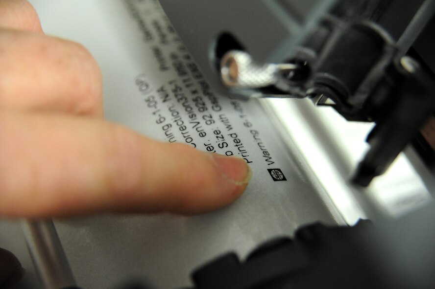 Bernard Jones, 509th Civil Engineer Squadron sign maker, ensures the blade of a plotter machine lines up with the material being cut for a sign, Whiteman Air Force Base, Mo., March 11, 2013. Almost every sign on base has been cut using this machine. (U.S. Air Force photo by Staff Sgt. Nick Wilson/Released)