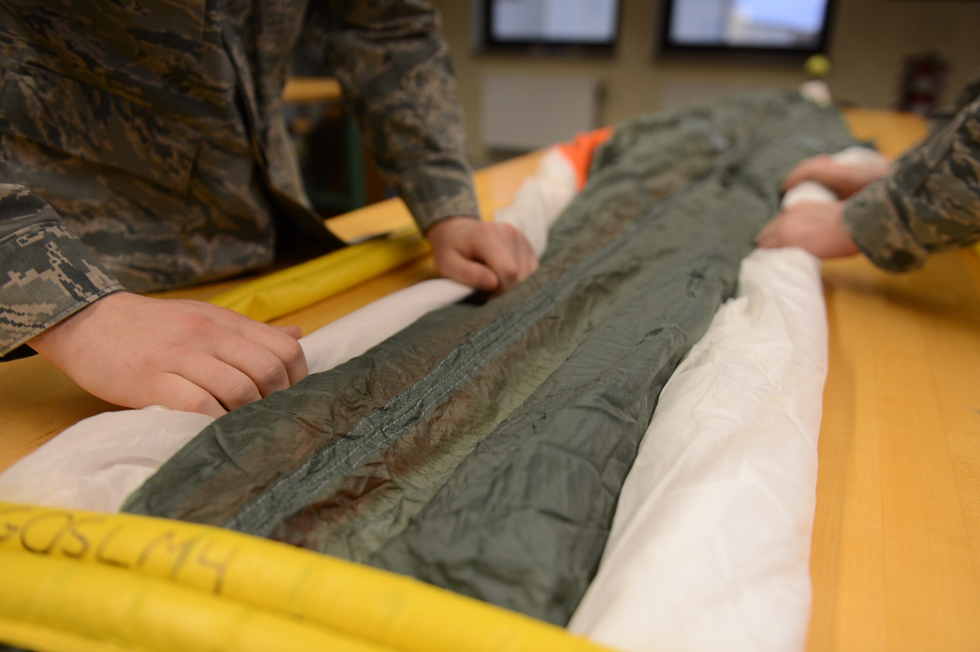 SPANGDAHLEM AIR BASE, Germany – U.S. Air Force Airman 1st Class Remington Murphy, 52nd Operations Support Squadron aircrew flight equipment technician from Richland, Wash., and Airman 1st Class Daniel Sisler, 52nd OSS aircrew flight equipment technician from Somerset, Wis., roll a parachute in preparation for packing March 20, 2013. Airmen check for tears, rips, cuts, fraying or any damage to the fabric to ensure the parachute is safe. (U.S. Air Force photo by Airman 1st Class Gustavo Castillo/Released)