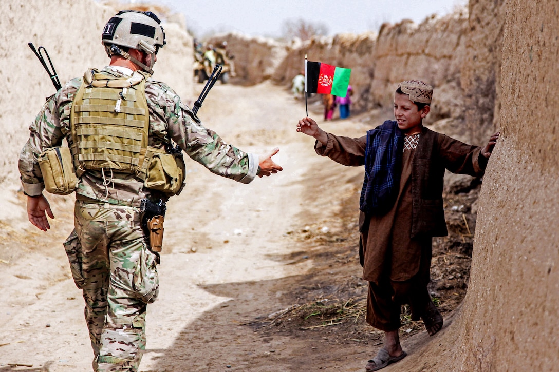 An Afghan child waves a flag at a member of coalition forces as he patrols to a medical clinic led by Afghan national security forces in the Panjwai district of Afghanistan’s Kandahar province, March 12, 2013. Coalition and Afghan forces held the clinic to promote improved security, governance and development.