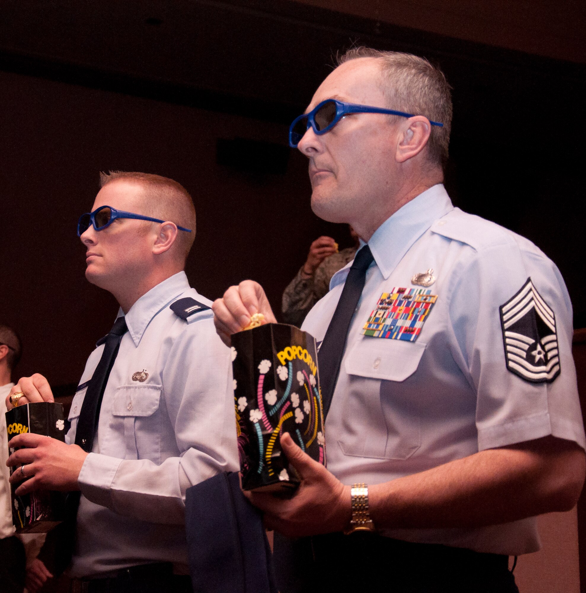 Capt. Stephen Hodgson, 90th Force Support Squadron operations officer, and Chief Master Sgt. Gerry Hires, 90th FSS chief enlisted manager, eat popcorn while watching a demonstration of the F. E. Warren Base Theater’s capability of showing 3D movies March 15. The ability to play movies in 3D is a result of their recent conversion from a movie reel projector to a digital projector.  (U.S. Air Force photo by Airman 1st Class Jason Wiese)