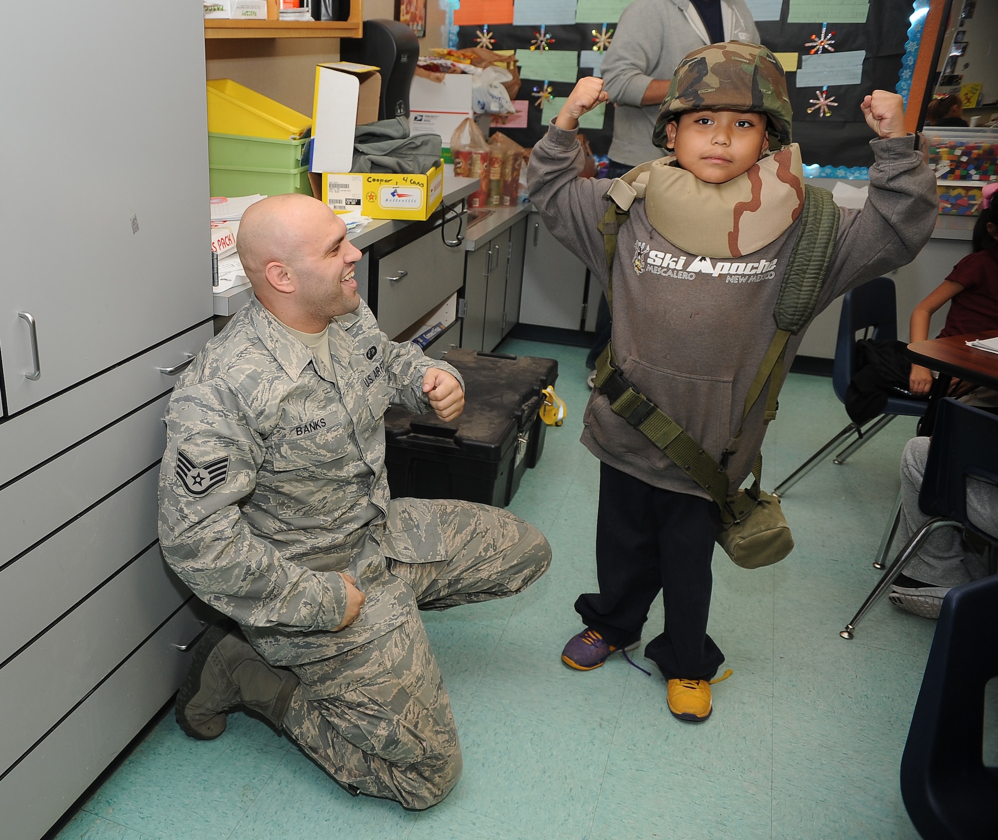 Staff Sgt. Michael Banks, 56th Contracting Squadron contracting officer, assists kindergartners with donning deployment gear March 8 at Littleton Elementary School in Avondale. Banks was one of many volunteers to visit the children during the school’s community day. (U.S. Air Force photo/Airman 1st Class James Hensley)