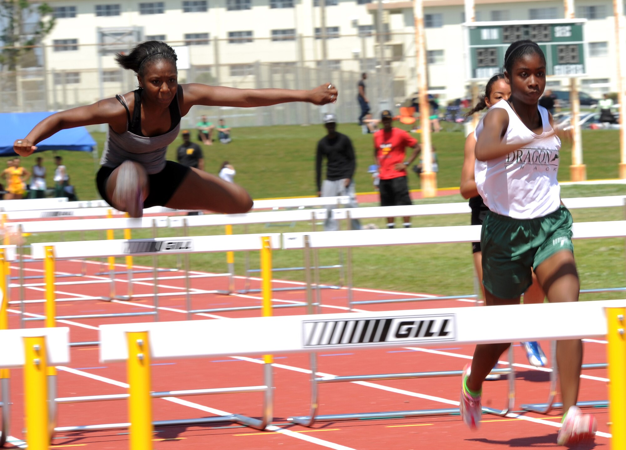U.S. Air Force Airman Rykeesha Barton (left) leaps over a hurdle to chase down her competition in the 100m hurdles during the first-ever island-wide track meet hosted by the Air Force Sergeants Association, Chapter 1553, on Kadena Air Base, Japan, March 23, 2013. The meet featured more than 15 events for men and women, as well as more than 10 events for youth aged 10 and older. (U.S. Air Force photo/Staff Sgt. Laszlo Babocsi)