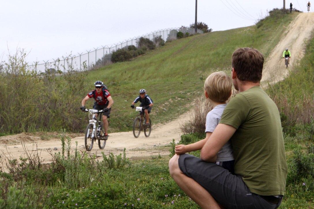 Justin Hillier and his 2-year-old son, Levi, watch Hell Fire Fat Tire Bike Race competitor’s race March 23. “I ride with some of these guys for (physical training),” said Hillier, the Geospatial Analyst and RRS manager with Remote Services-Marine Corps NST for National Geospatial-Intelligence Agency.