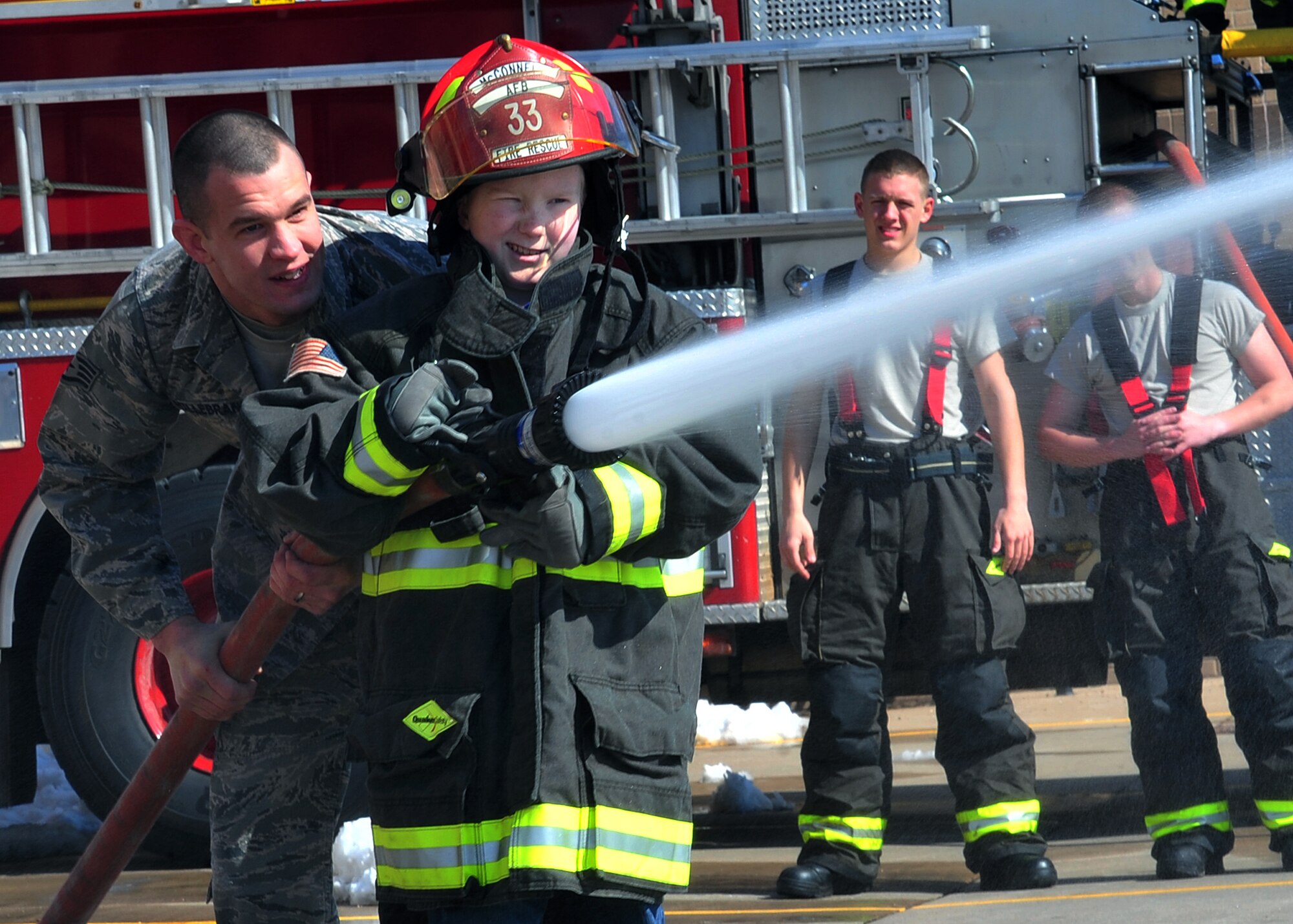 Staff Sgt. Bradley Hillebrand, 22nd Civil Engineer Squadron fire station captain, assists Micah Wemmer, honorary 22nd Operation Support Squadron “Mighty Eagle”, with a fire hose March 25, 2013, McConnell Air Force Base, Kan. Wemmer was visiting McConnell AFB as part of the “Pilot for a Day” program. This program invites children with serious or chronic medical conditions to be a guest of the 22nd Air Refueling Wing and one of the flying squadrons for a day. (U.S Air Force photo/Senior Airman Katrina M. Brisbin)