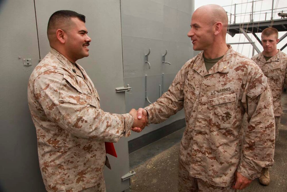 Gunnery Sgt. Raul O. Chapa (left), radio chief, Command Element, 15th Marine Expeditionary Unit, shakes hands with Maj. Keith Kovats, the unit's communications officer, after re-enlisting on USS Peleliu, March 20. Chapa, 34, is from San Antonio, Texas, and joined the Marine Corps for a challenge to be a part of the best. He chose communications because it enabled him to be close to the infantry, and he was interested in the technology aspect. To pass the time on deployment, he enjoys going to the gym daily and spending time with his Marines. His favorite part of the deployment has been serving with the Command Element because it allowed him to gain a new perspective of the Marine Air-Ground Task Force. He is looking forward to spending time with his family the most when he returns home. The 15th MEU is deployed as part of the Peleliu Amphibious Ready Group as a U.S. Central Command theater reserve force, providing support for maritime security operations and theater security cooperation efforts in the U.S. 5th Fleet area of responsibility. (U.S. Marine Corps photo by Cpl. John Robbart III/Released)