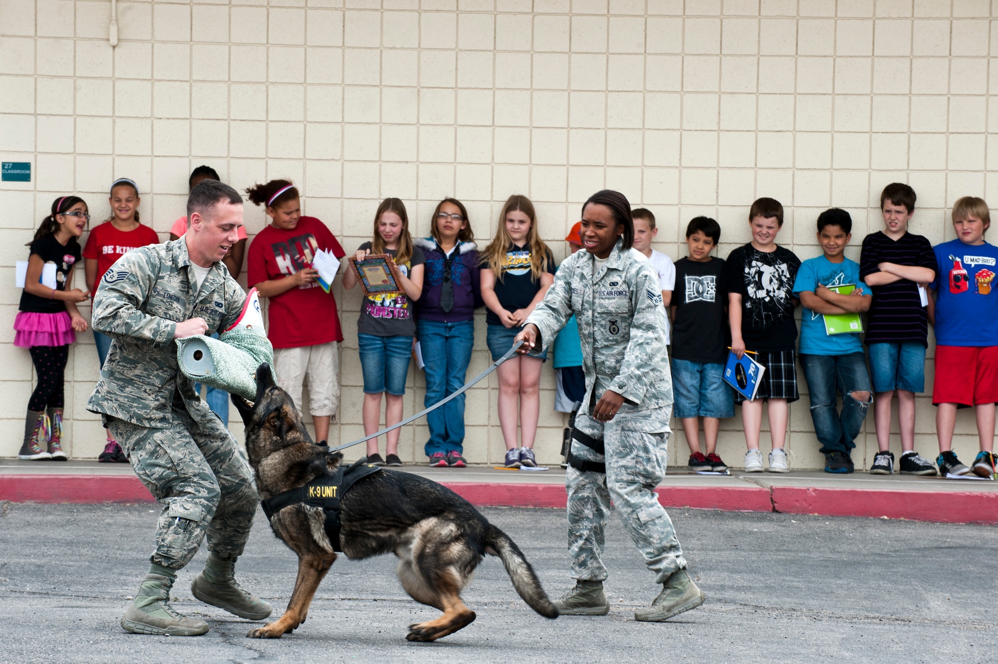 Staff Sgt. Matthew Lenegan and Senior Airman Kiara Dykes, 99th Security Forces military working dog handlers, conduct a military working dog demonstration for Lomie Heard Elementary school students March 20, 2013, at Nellis Air Force Base, Nev. Lenegan and Dykes demonstrated various commands used with the dogs to apprehend a suspect. (U.S. Air Force photo by Airman 1st Class Jason Couillard)
