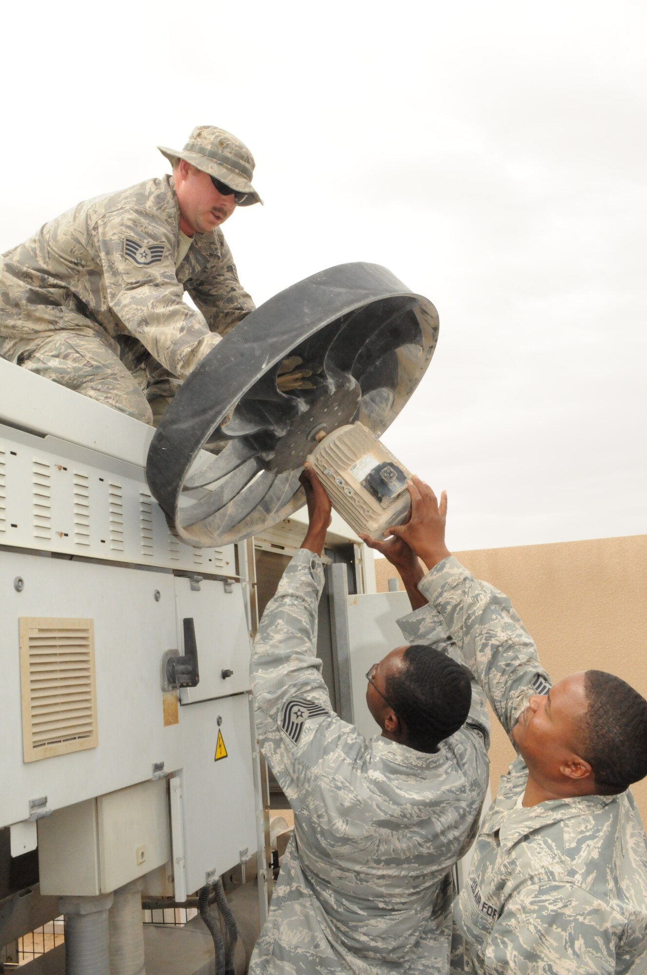 SOUTHWEST ASIA -- Staff Sgt. James Upton lowers a bad condenser chiller fan motor to Tech. Sgt. Michael Jones and Staff Sgt. Edward Reed after replacing it with a new one, March 21. The 379th Expeditionary Civil Engineer Squadron Heating Ventilation Air Conditioning / Refrigeration shop maintains all wing and tenant HVAC/R systems on base. (U.S. Air Force photo/Master Sgt. Christian Michael)