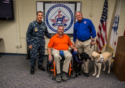 Commander Chadwick Bryant, Naval Consolidated Brig Charleston commander, and Rick Hairston, Canines for Service president, present service dog Malachi (black Labrador) to Rick Hayes, an Air Force veteran, during a ceremony March 21, 2013, at the Naval Consolidated Brig Charleston on Joint Base Charleston – Weapons Station, S.C. CFS is a non-profit health and human services organization that trains service dogs for people with disabilities. Through this program, military prisoners are taught to train service dogs for veterans with disabilities. Since the program's inception, 15 wounded service members have received service dogs. Service dogs are constant companions and can assist veterans with more than 70 tasks, including retrieving and carrying objects, opening doors, and helping with stress and balance difficulties.. (U.S. Air Force photo/ Senior Airman George Goslin)