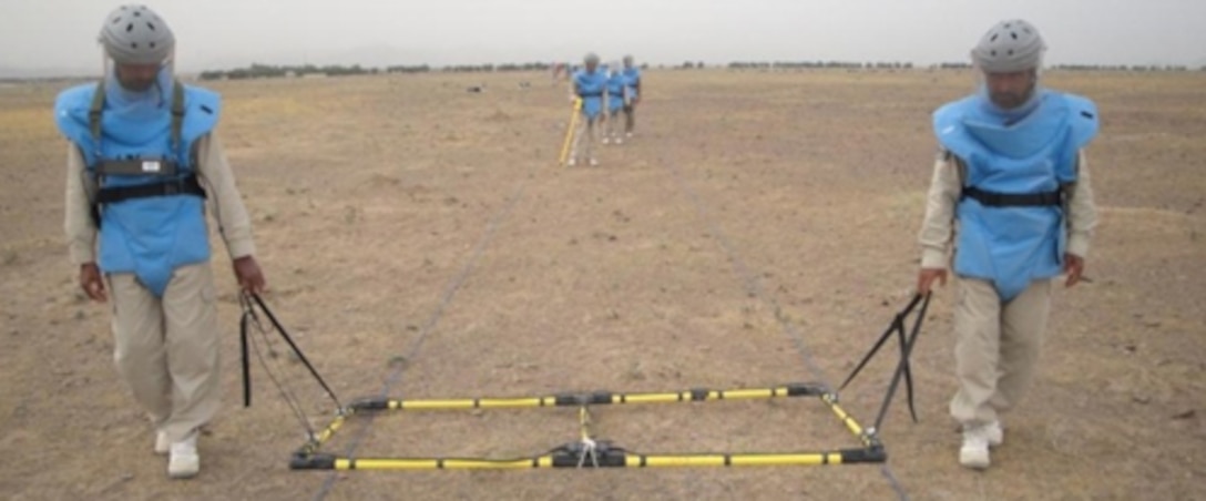 Local technicians survey land near the Shin Dand Airport in Afghanistan using an Ebinger LLD (Large Loop Detector) to search for hazardous material.