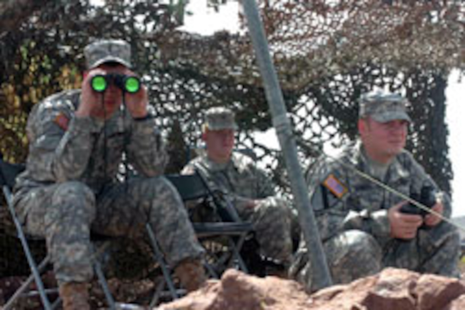 Under Cover. 2nd Lt. Brian Inman (left), of Fayetteville, Ark., Spc. Matthew Bealer (center), from Branson, Mo., and Sgt. Jay Sanders (right), from Hot Springs, Ark., take shelter from the bright New Mexico sun under the camouflage netting of their mountain top observation point. The Soldiers, members of the Arkansas National Guard's 39th Infantry Brigade Combat Team, are part of Task Force Arkansas participating in Operation Jump Start along the U.S. border with Mexico. From their outpost nearly 1,000 feet above the dessert floor, Inman, Bealer and Sanders can monitor movement in the desert on one side, vehicles along a major highway on a second side, and suspicious "stow aways" aboard railroad cars on a third side.