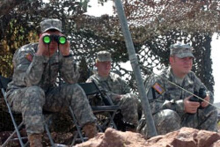 Under Cover. 2nd Lt. Brian Inman (left), of Fayetteville, Ark., Spc. Matthew Bealer (center), from Branson, Mo., and Sgt. Jay Sanders (right), from Hot Springs, Ark., take shelter from the bright New Mexico sun under the camouflage netting of their mountain top observation point. The Soldiers, members of the Arkansas National Guard's 39th Infantry Brigade Combat Team, are part of Task Force Arkansas participating in Operation Jump Start along the U.S. border with Mexico. From their outpost nearly 1,000 feet above the dessert floor, Inman, Bealer and Sanders can monitor movement in the desert on one side, vehicles along a major highway on a second side, and suspicious "stow aways" aboard railroad cars on a third side.