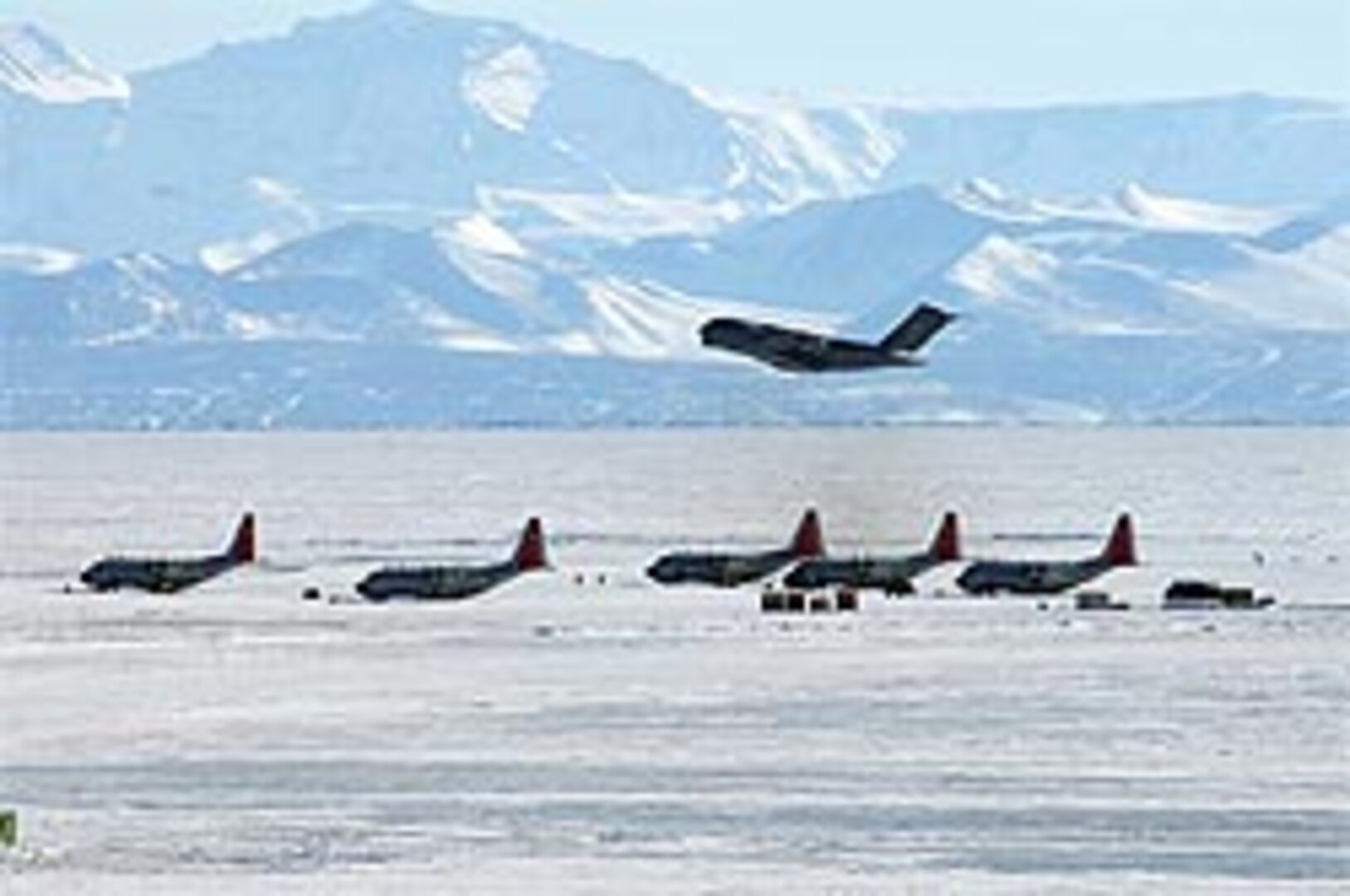 A C-17 cargo jet takes off from an ice runway at McMurdo Station in Antarctica over five LC-130s parked on a sea ice ramp.