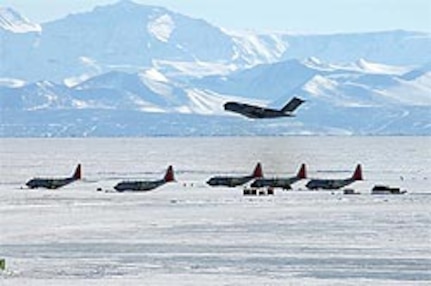 A C-17 cargo jet takes off from an ice runway at McMurdo Station in Antarctica over five LC-130s parked on a sea ice ramp.