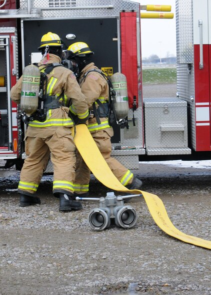 100th Civil Engineer Squadron Fire Department firefighters set up a fire hose during an exercise March 25, 2013, at RAF Mildenhall, England. The scenario involved lightning striking a building, which caused a fire. A person ran out of the building and got hit by a car, which then hit another car, turning it upside down and trapping three people. Firefighters prioritized their response, as the vehicle accident was a risk to life, while the building wasn't considered mission-essential. The first responders rescued the simulated victims from the vehicle and transported them to safety until medics appeared on-scene. (U.S. Air Force photo by Gina Randall/Released)