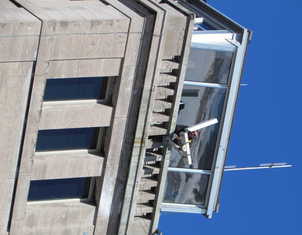 Working in a fall protection harness nearly 75 feet above the ground, an electrician cleans and prepares to reposition the east facing camera on the control tower at the Soo Locks.
