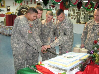 Spc. Eric Varela, Pfc. Randy Demand and Pfc. Joseph Levesque (left to right) demonstrate their cake-cutting prowess with Brig. Gen. Douglas Earhart, commander of Multi-National Task Force (East), during the unit's observation of the 370th birthday of the National Guard. Each of the Soldiers is the youngest member of one of the three oldest units in the Army, all of which are serving in Kosovo as part of Operation Joint Guardian.