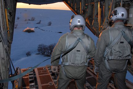 Wyoming Air National Guard loadmasters aboard a C-130 Hercules aircraft watch as a 1-ton hay bale lands near a herd of cows during an emergency feeding mission in southeast Colorado Jan. 3, 2007. The hay is being dropped near La Junta, Colo., to help feed livestock that have been stranded from a snow storm that has impacted the area.