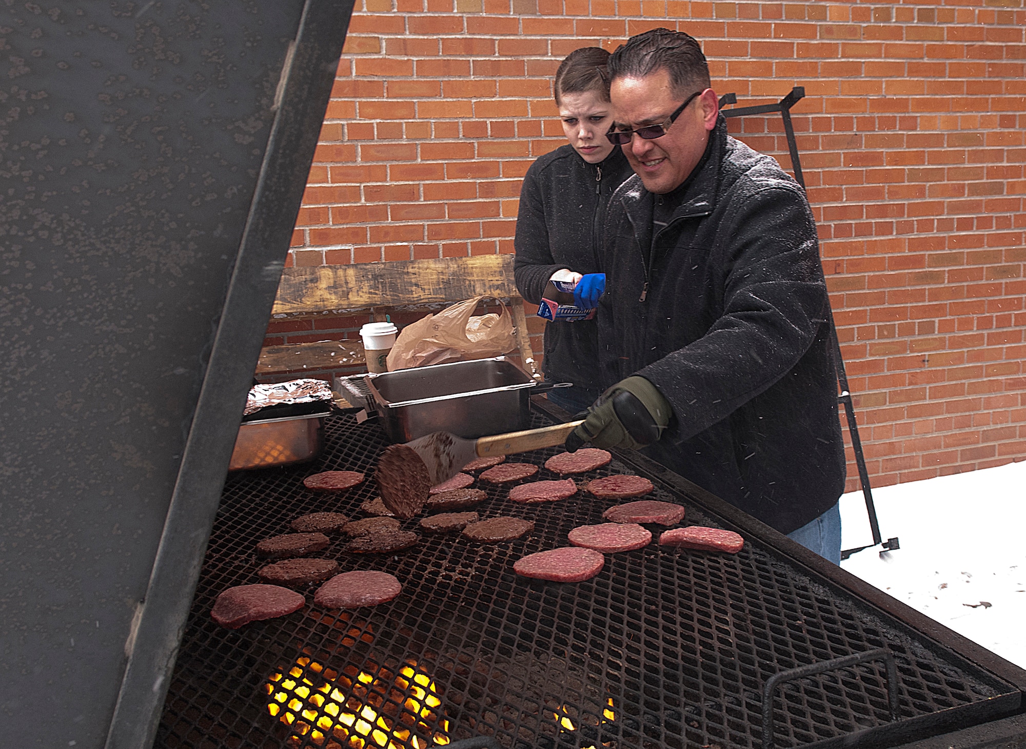 The F. E. Warren Air Force Base Spring Carnival goes on in spite of blowing snow as Master Sgt. Jaime Garcia, 90th Missile Security Forces Squadron, and Senior Airman Katie Herrington, 90th Force Support Squadron, work the grill outside the Fall Hall Community Center March 23. The burgers and hot dogs fed the Airmen and their families taking part in the festivities inside the hall. (U.S. Air Force photo by R.J. Oriez)