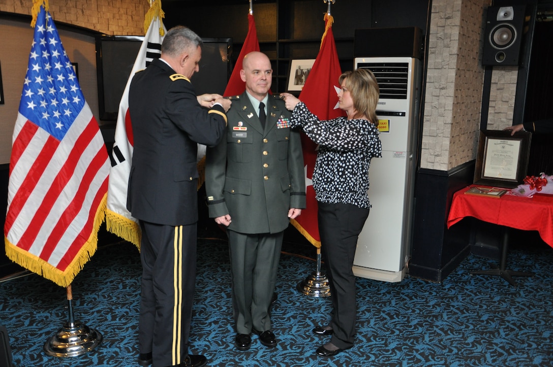 Col. Greg Baisch was promoted to his present rank by Lt. Gen. John D. Johnson, 8th Army commander (left) and his wife Mrs. Laurie Baisch (right). The eagle rank insignias they are pinning on him had been worn by his father during his Air Force career. Far East District commander Col. Donald E. Degidio, Jr., also presented Baisch with the de Fleury medal, an award of the US Army Engineer Association, which recognizes outstanding contributions to the engineering regiment.  